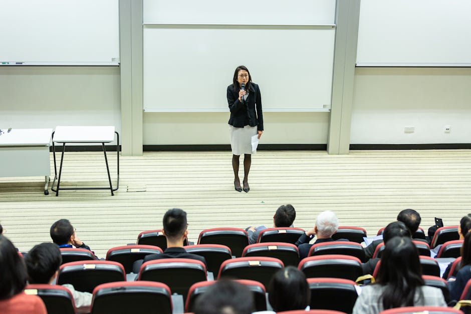 Female speaker presenting to an audience in a modern auditorium setting